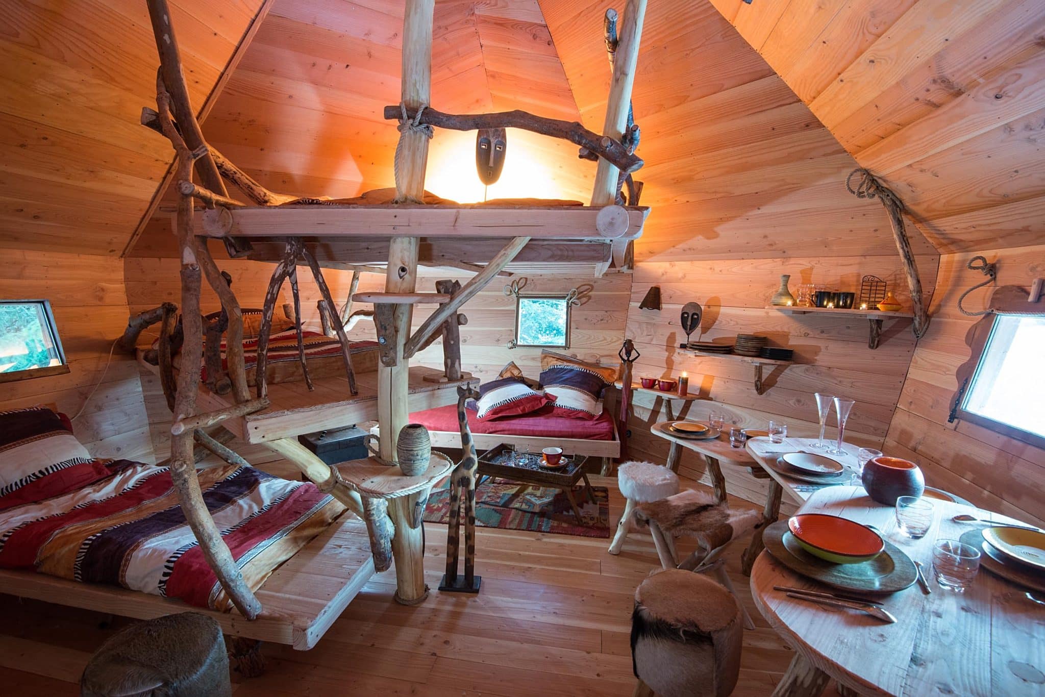 photo intérieure de la tribu perchée avec un espace commun avec des lits et une table de repas installé avec assiettes, verres et couverts