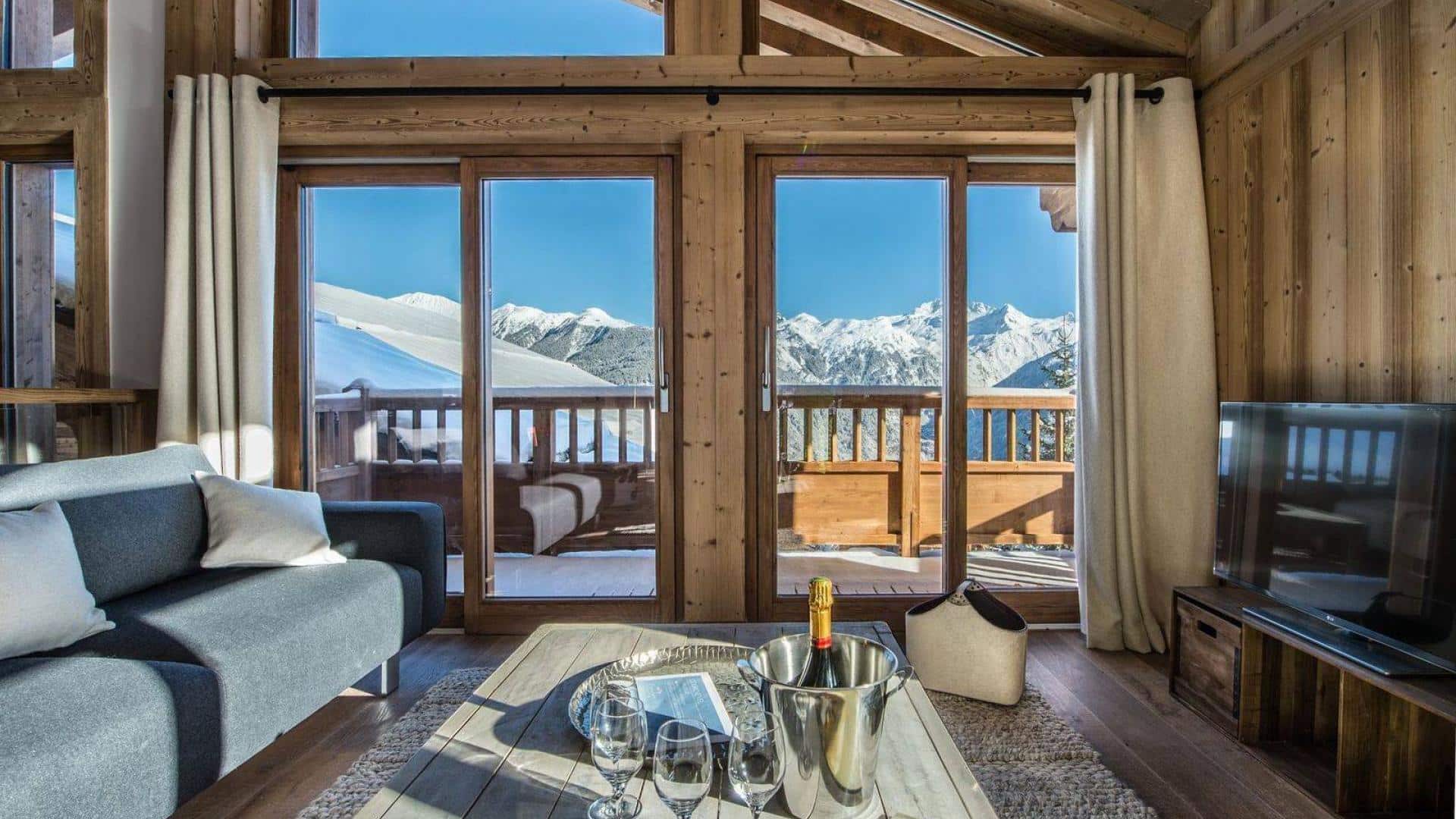 photo du chalet anika depuis le salon avec la vue sur les montagnes et la terrasse. sur la table basse, le champagne est disposé avec des flutes.