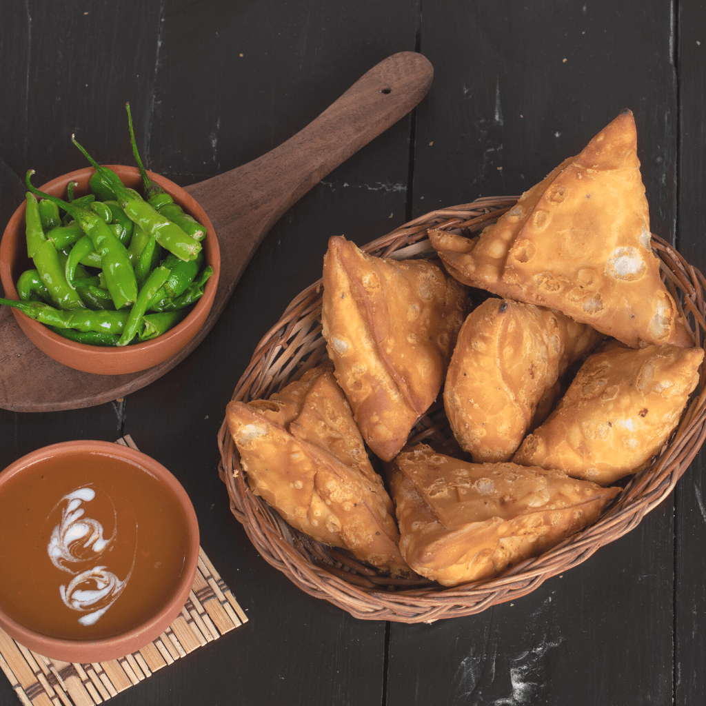 Panier de samousa à côté d'un bol de piment vert et d'une sauce orange