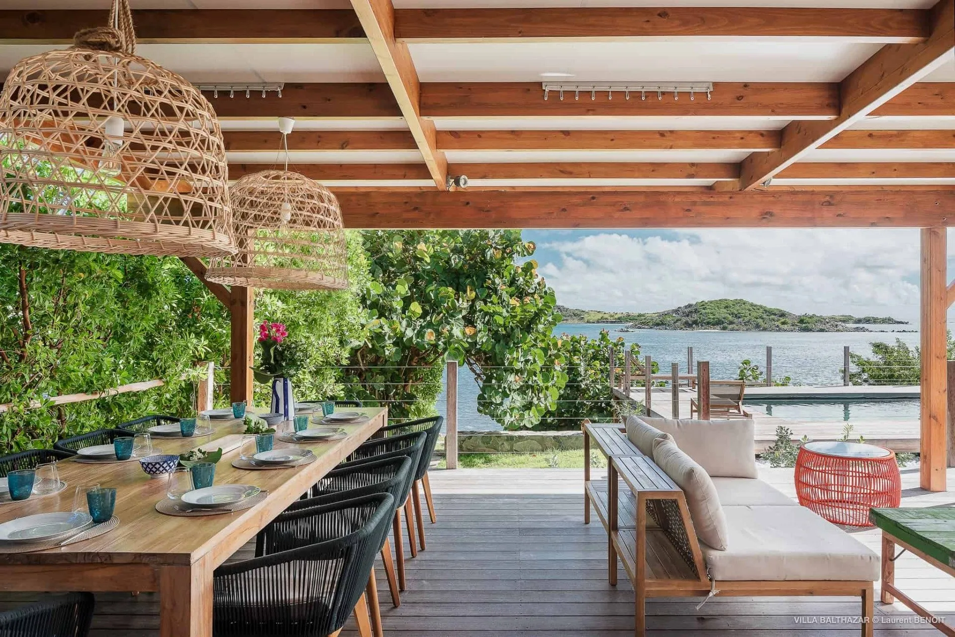 terrasse extérieure couverte avec table pour le repas, chaises et la table est dressée avec vaisselle et vue sur la mer avec piscine privée